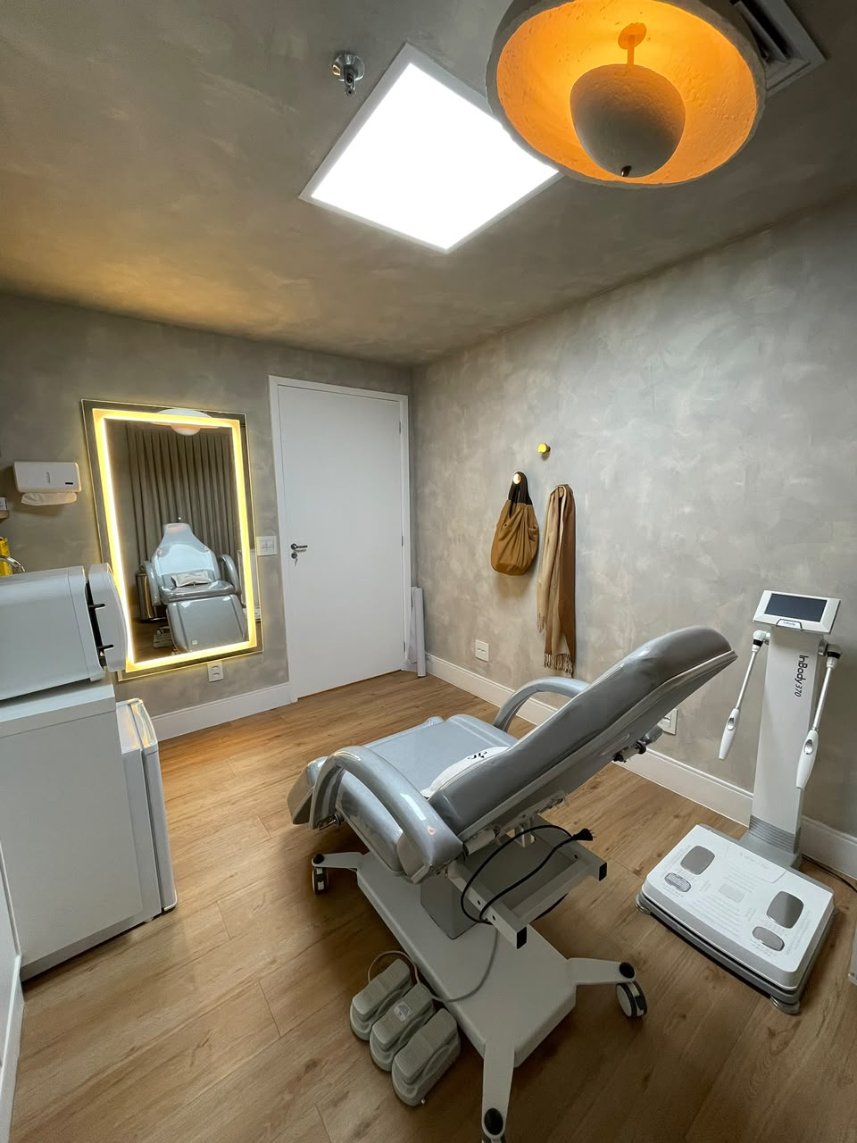 Sala de avaliação corporal com maca e equipamento de bioimpedância